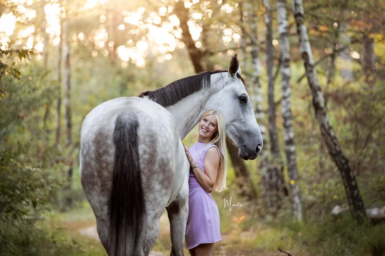 Marit van Wees leunt glimlachend tegen de hals van haar paard Co in een bos met berken.